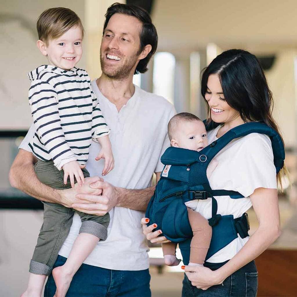 bebe dans porte bebe bleu face a sa maman papa et frere